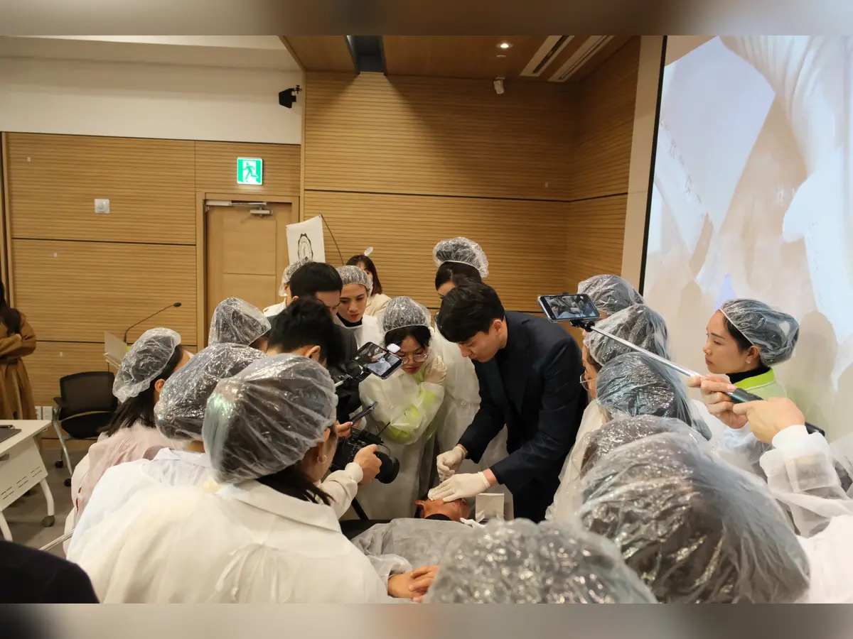 Học viên đội mũ và mặc áo bảo hộ tập trung quanh bàn thực hành cùng người hướng dẫn.